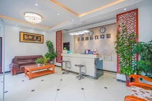 A hotel lobby with a reception desk, a sofa, a coffee table, and a clock on the wall. - Qianyi Inn (Yichang)