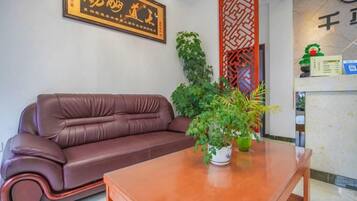 Un sofá de cuero marrón, una mesa de madera con una planta en maceta y un panel decorativo en la pared.
