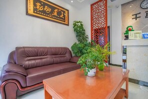 Un sofá de cuero marrón, una mesa de madera con una planta en maceta y un panel decorativo en la pared.