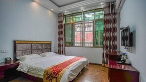A bedroom with a bed, a wooden floor, a window with curtains, a TV, and a small table with a kettle. - Qianyi Inn (Yichang)