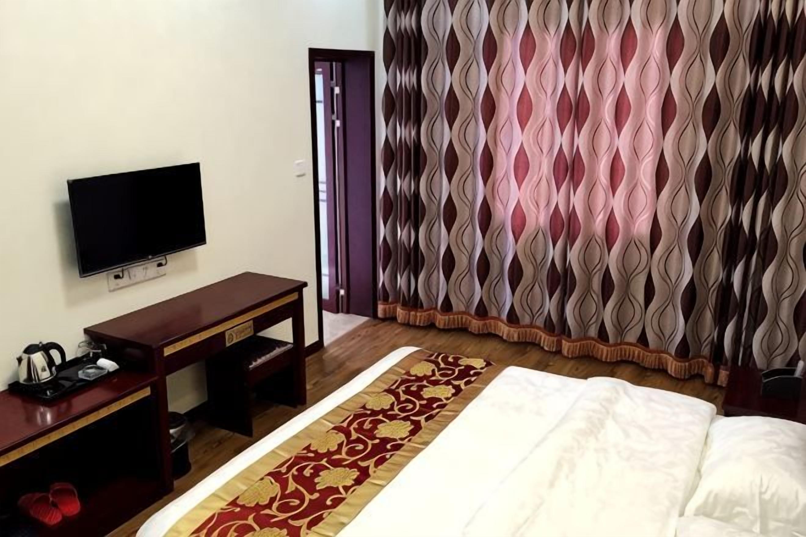 A hotel room with a bed, a television, a desk, and a patterned curtain.
