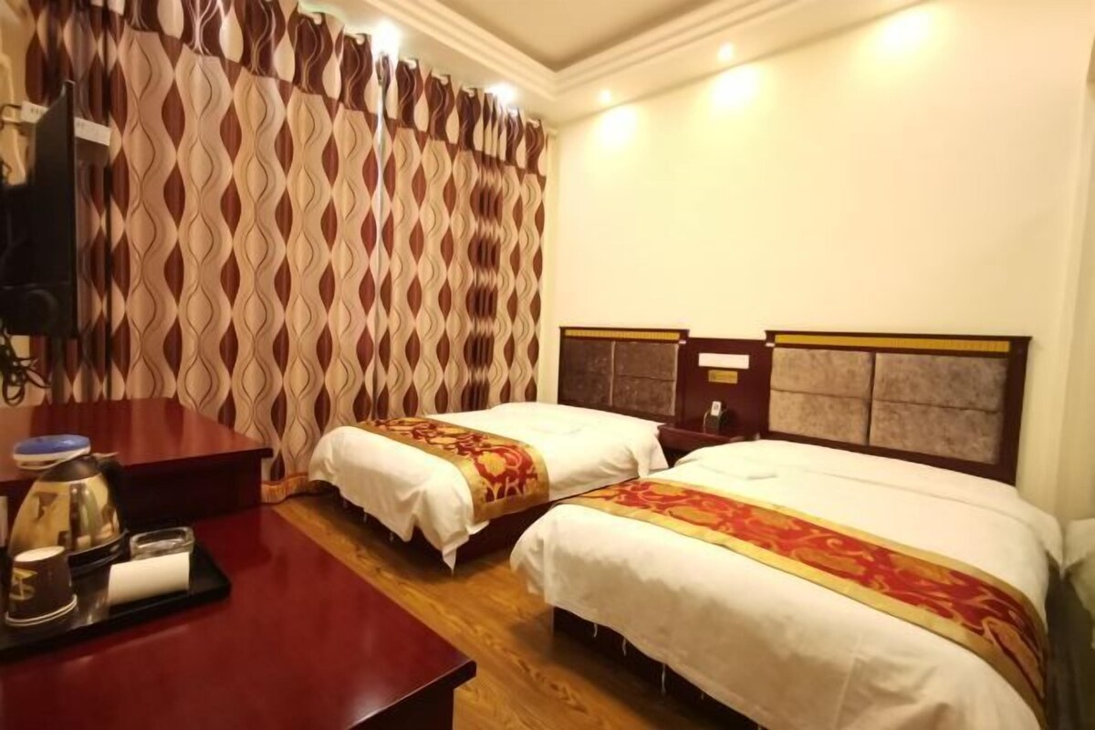 A hotel room with two beds, a wooden desk, a coffee maker, and a patterned curtain.