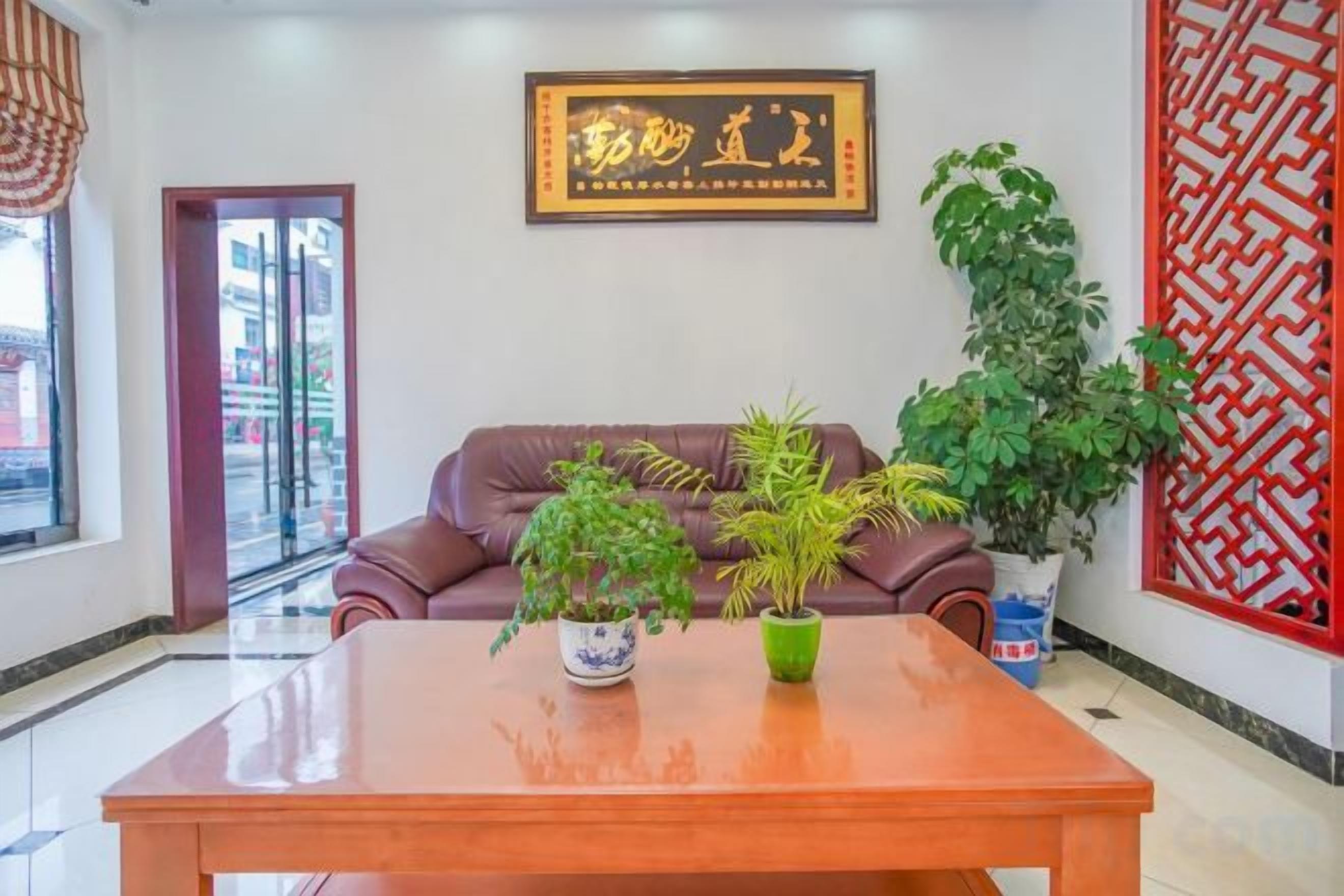 Una habitación con un sofá de cuero marrón, una mesa de madera con plantas en macetas y un biombo decorativo rojo.