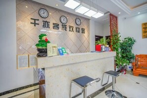 A reception desk with clocks, a potted plant, and a seating area. - Qianyi Inn (Yichang)