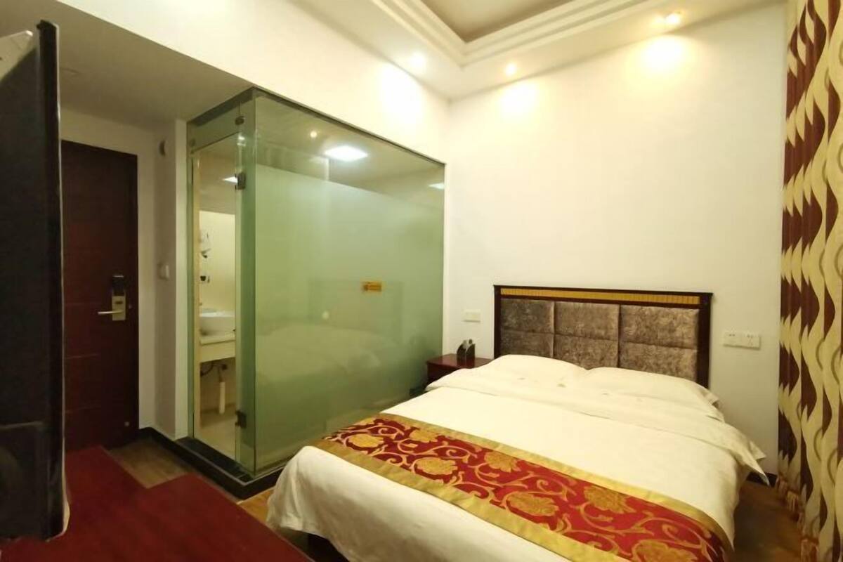 A hotel room with a bed, a glass-enclosed shower, a wooden door, and a patterned curtain.