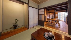 A traditional Japanese room with tatami flooring, a low wooden table with a tray of tea and a teapot, sliding doors, and a view of a dining area with a wooden table and chairs. - Kyoto 11 Inn Shimabara (Kyoto)