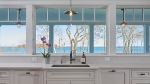 A kitchen with a large window, a sink, and a vase with flowers. - Waterfront estate near Portland with pool, dock and sweeping views of Casco Bay. (Yarmouth)