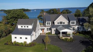 A large, two-story house with a covered porch and a view of the water. - Waterfront estate near Portland with pool, dock and sweeping views of Casco Bay. (Yarmouth)