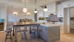 A modern kitchen with a central island, bar stools, pendant lighting, and white cabinetry. - Waterfront estate near Portland with pool, dock and sweeping views of Casco Bay. (Yarmouth)