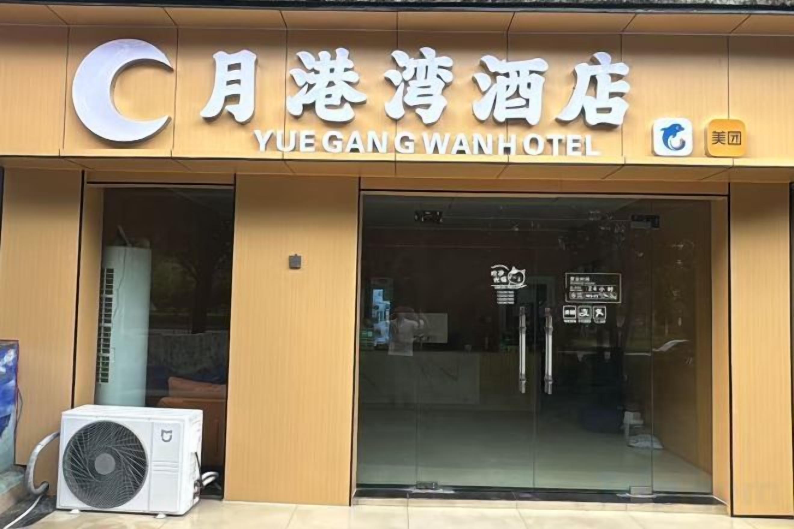 The exterior of the Yue Gang Wan Hotel with a clear entrance, a signboard, and a fan outside.
