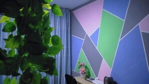Una habitación con pared de diseño geométrico, un escritorio con una silla, una planta en maceta y un pequeño florero con flores.