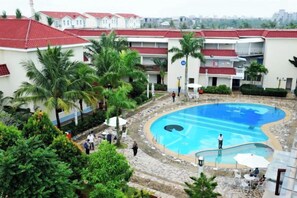 A swimming pool surrounded by palm trees and a building with red roofs. - Shanhai Holiday Resort (Haikou)