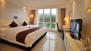 A hotel room with a large bed, a TV, a desk with a lamp, and a window with curtains. - Shanhai Holiday Resort (Haikou)