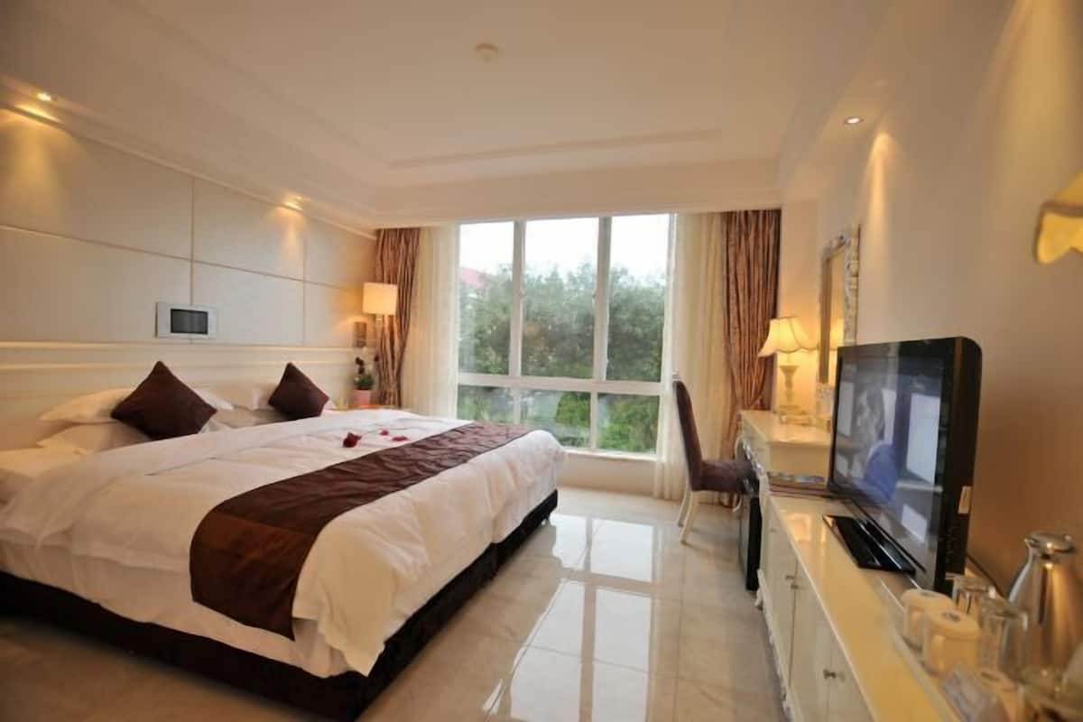 A hotel room with a large bed, a TV, a desk with a lamp, and a window with curtains.
