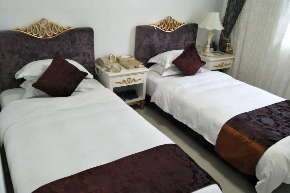A hotel room with two beds, each with a headboard, bedside tables, lamps, and pillows.