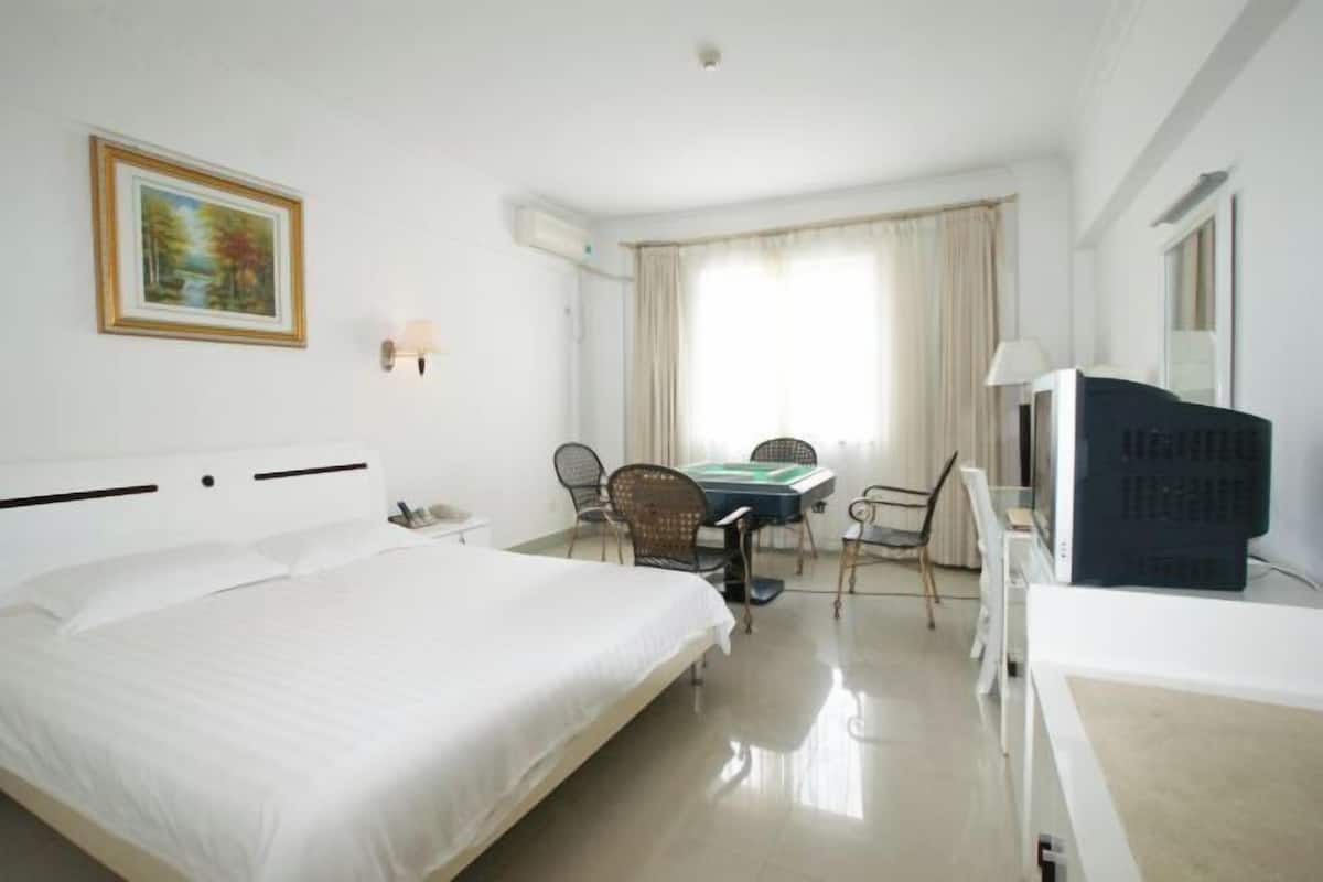 A hotel room with a large bed, a desk with chairs, a television, and a painting on the wall.