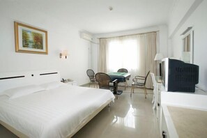 A hotel room with a large bed, a desk with chairs, a television, and a painting on the wall. - Shanhai Holiday Resort (Haikou)