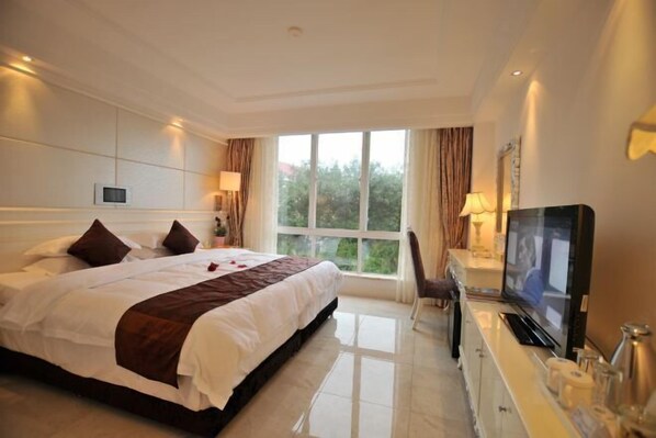 A hotel room with a large bed, a television, a desk with a computer, and a window with curtains. - Shanhai Holiday Resort (Haikou)