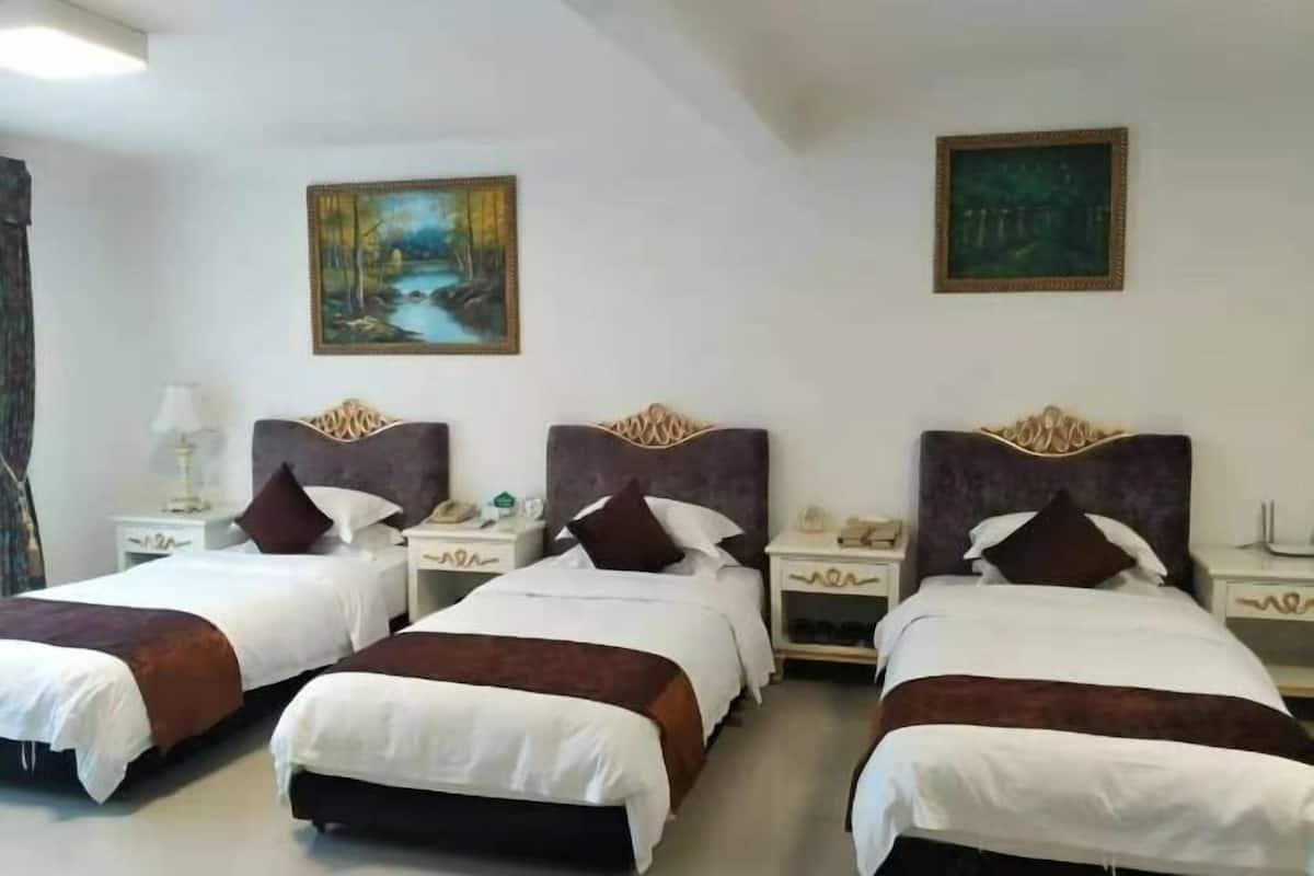 A hotel room with three beds, each with a headboard, bedside tables, and a painting on the wall.