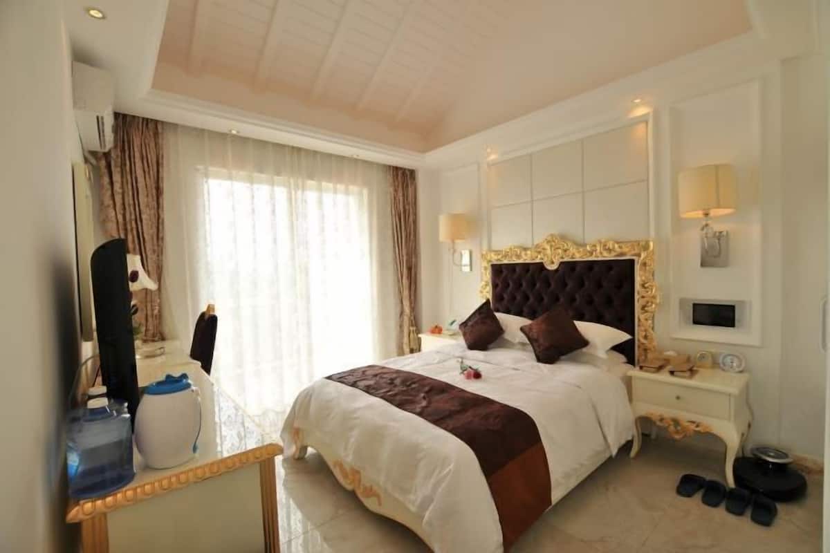 A hotel room with a large bed, a bedside table, a mirror, and a window with curtains.