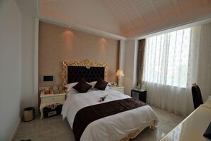 A hotel room with a large bed, a nightstand with a lamp, a TV, and a window with curtains. - Shanhai Holiday Resort (Haikou)