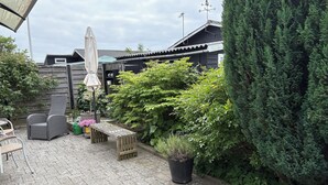 Une terrasse avec des meubles d’extérieur, une plante en pot et une clôture en bois.