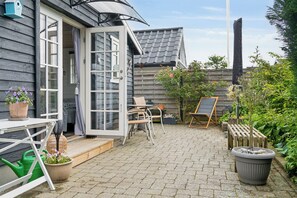 A patio with a table, chairs, a potted plant, a green watering can, and a wooden bench.