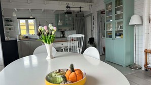 Un coin repas avec une table blanche, un bol jaune rempli de fruits et un vase avec des fleurs.