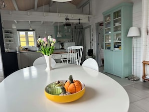 Et spiseområde med et hvidt bord, en gul skål med frugt og en vase med blomster.