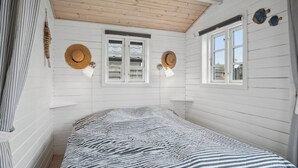 A bedroom with a striped bedspread, two windows with shutters, and two wall-mounted hats. - Holiday home close to the beach and restaurants (Karrebæksminde)