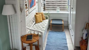 Une pièce chaleureuse avec un canapé blanc, une petite table, un tapis bleu et une fenêtre avec des stores.