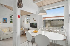 A white-walled room with a dining table, chairs, a sofa, and a TV.