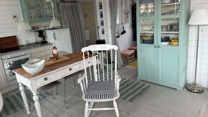 Une cuisine avec une table en bois, une chaise blanche, un meuble avec des portes en verre et un luminaire suspendu.