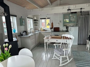 Une cuisine rustique avec un îlot central en bois, des meubles blancs et un coin repas agrémenté d’un fauteuil à bascule.