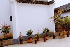 A white building with a tiled roof, potted plants, and a stone wall. - Jingxian Comfy Hotel (Jing County)