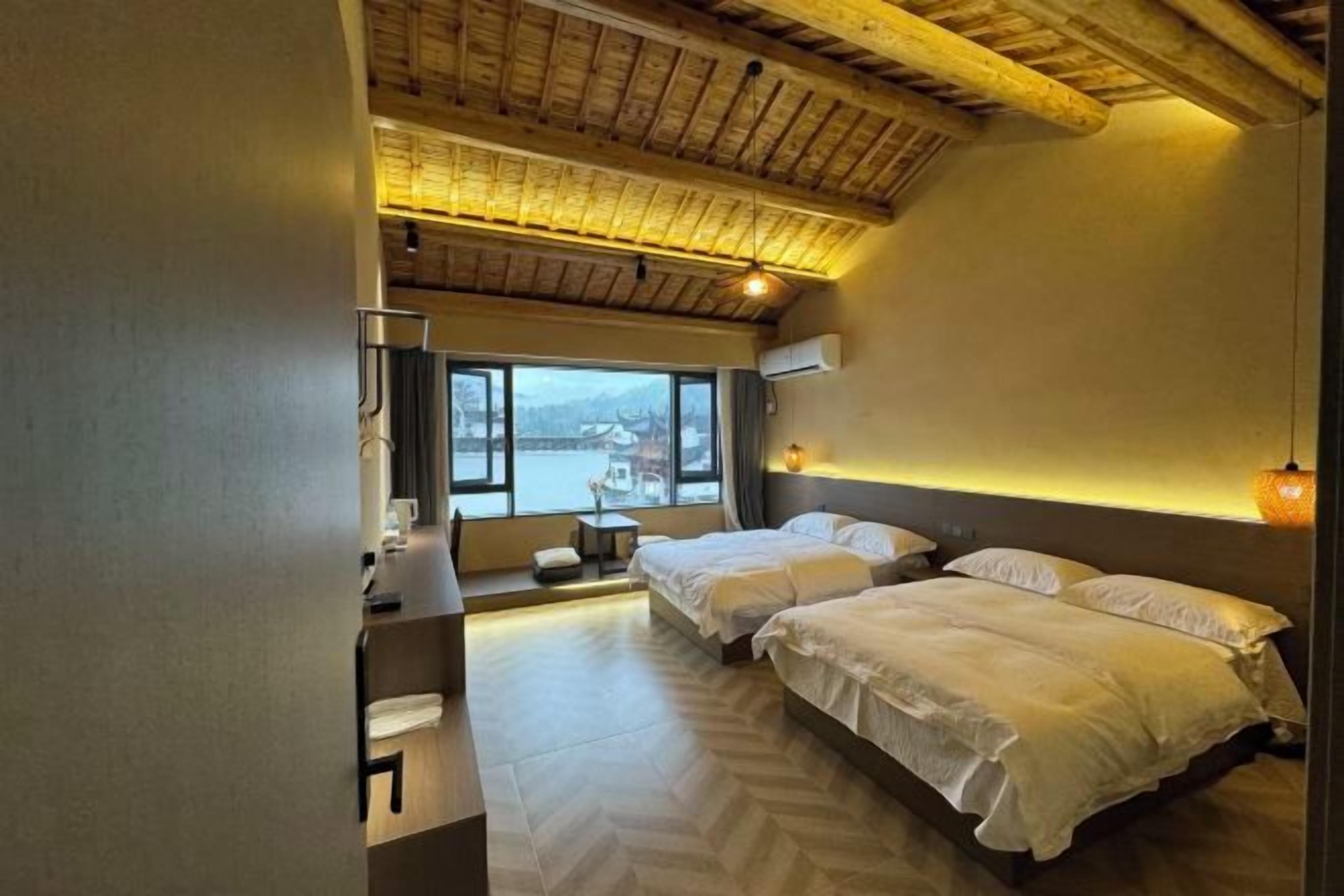 Habitación de hotel con dos camas, un escritorio, una silla, un ventanal con vistas y techo de madera.