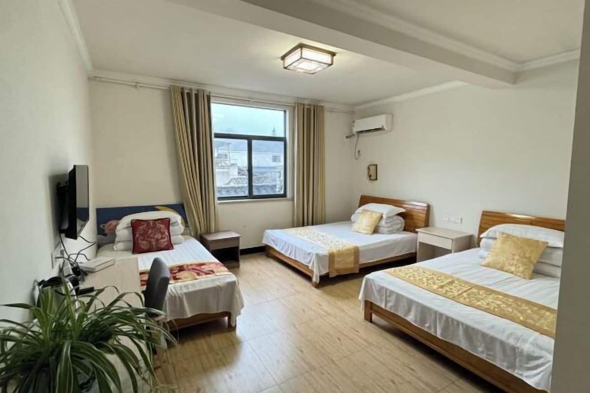 Habitación de hotel con tres camas, un televisor, una ventana con cortinas y una lámpara en el techo.