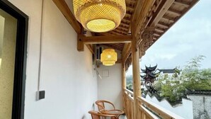 Un balcone con sedie in vimini, una ringhiera in legno e un edificio tradizionale cinese sullo sfondo.