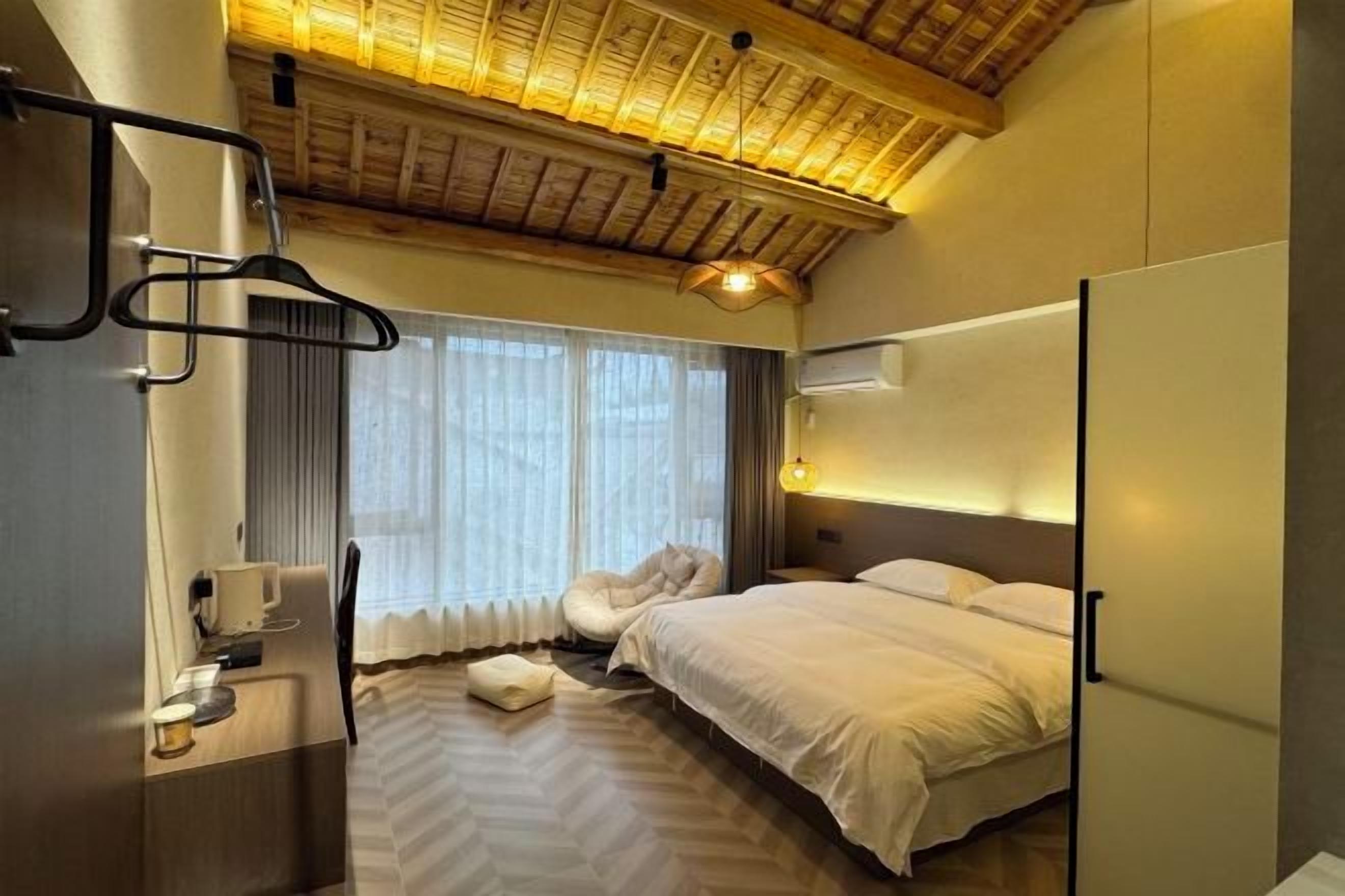Habitación de hotel con cama, escritorio, silla, lámpara colgante y ventana con cortinas.