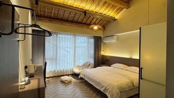 Habitación de hotel con cama, escritorio, silla, lámpara colgante y ventana con cortinas.