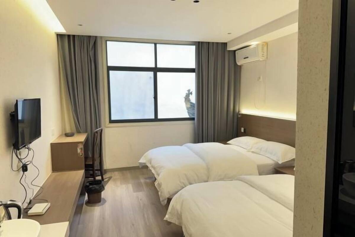 Habitación de hotel con dos camas, televisión, escritorio y ventana con cortinas.
