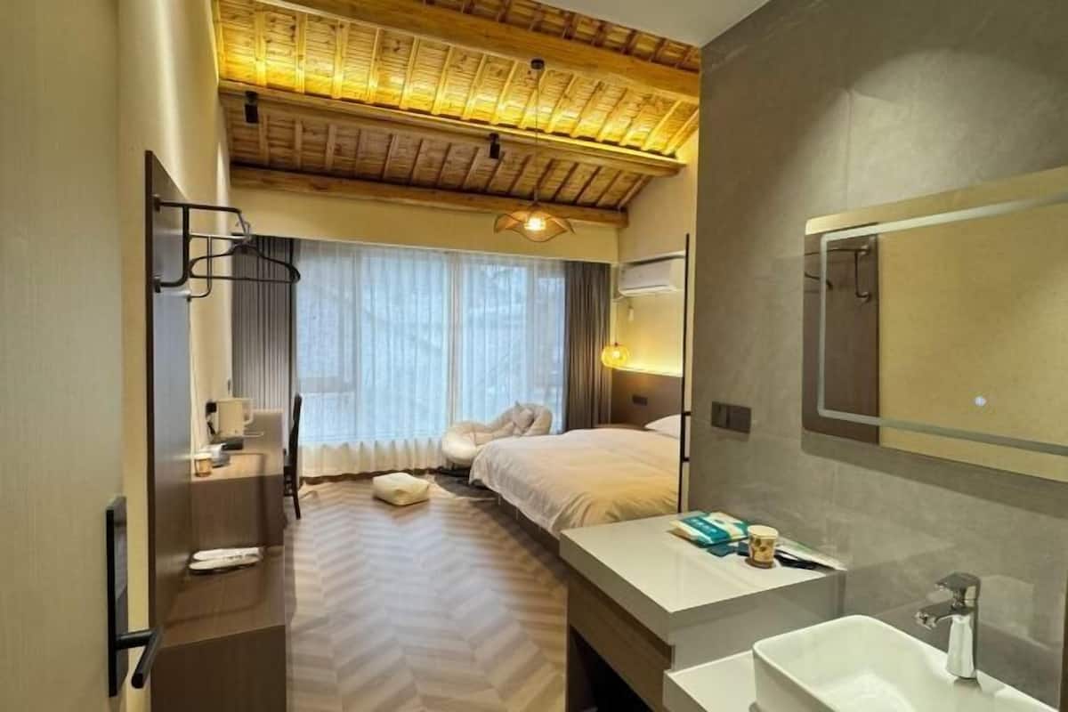 Habitación de hotel con cama, mesita de noche, espejo, lavamanos y ventana con cortinas.