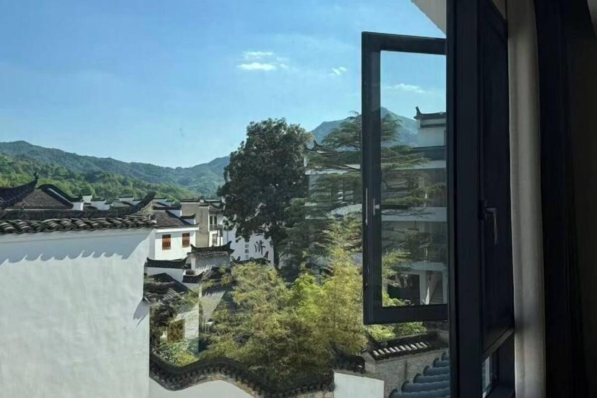 Un edificio tradicional con techo de tejas, rodeado de vegetación y montañas al fondo.