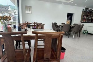 Un restaurante con mesas y sillas de madera, vista al exterior por la ventana, y una barra con distintos productos.