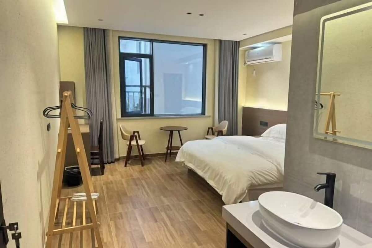 Una habitación de hotel con una cama, un baño con un lavamanos grande, una ventana con cortinas y una pequeña mesa con sillas.