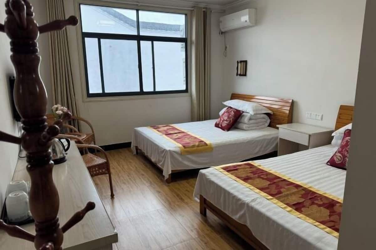 Habitación de hotel con dos camas, un escritorio de madera, una silla y una ventana con cortinas.
