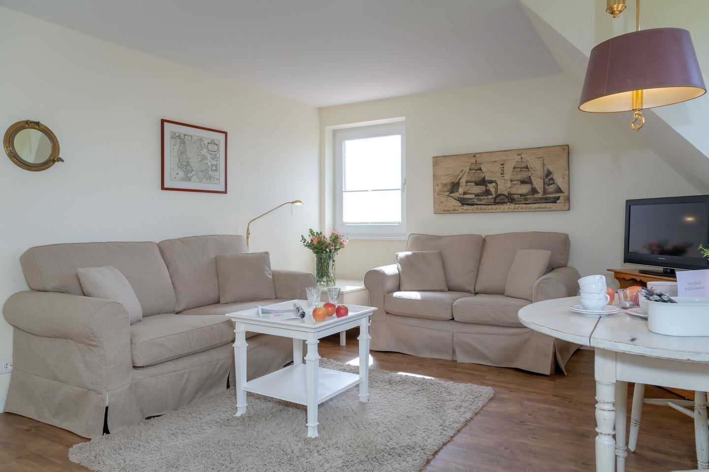 A living room with two beige sofas, a white coffee table, a small white side table, a round white table, a television, and a lamp.