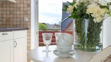 Eine Küche mit weißen Schränken, einem sechseckigen Fliesenboden, einem Esstisch mit Blumenvase und Blick durch eine Tür.