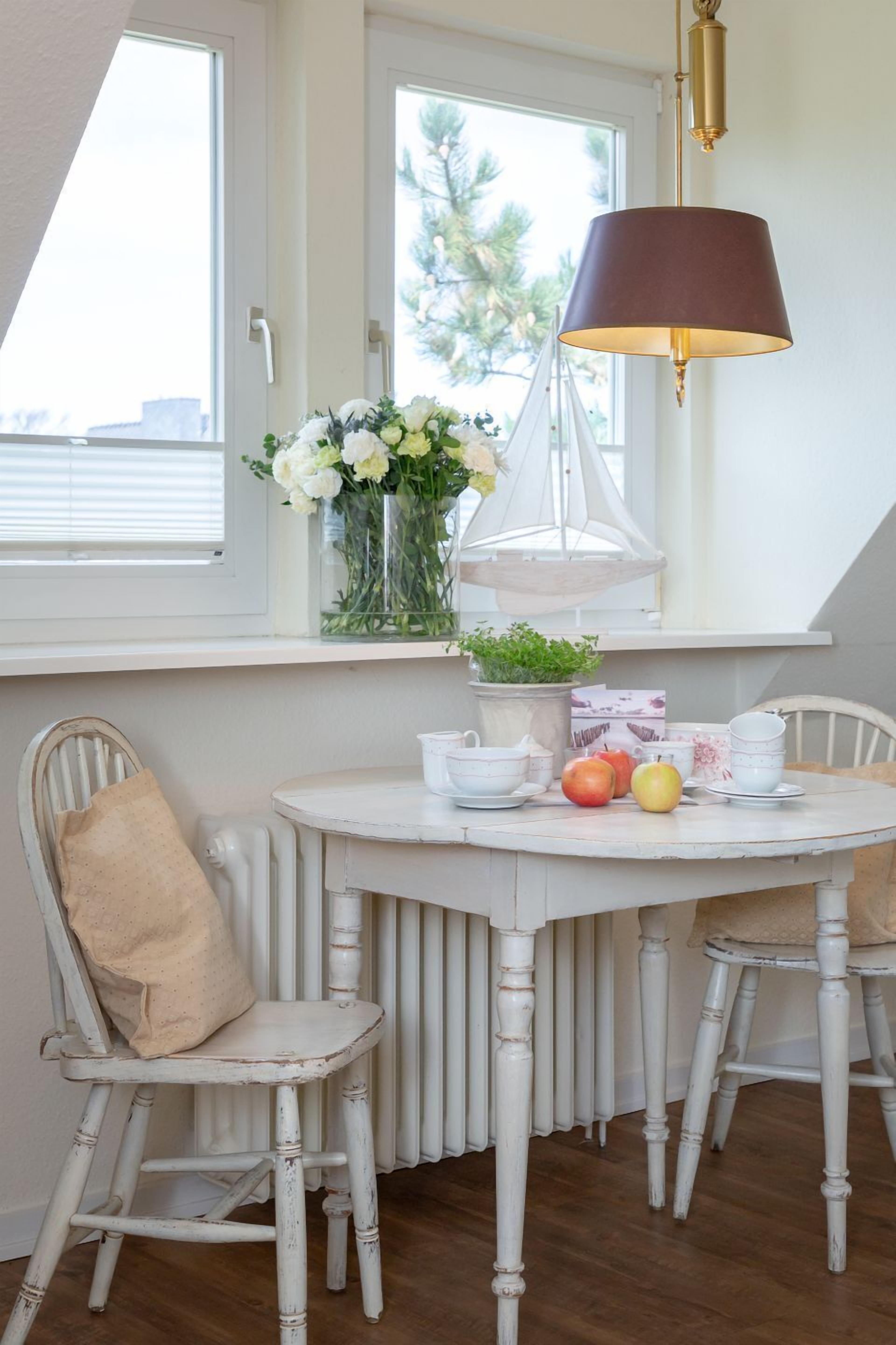 Ein weißer Esstisch mit Stühlen, eine Vase mit Blumen und eine Lampe.