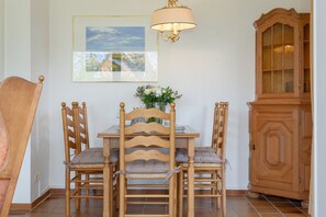 Ruokailutila, jossa on puinen pöytä ja tuolit, kattokruunu, kaappi ja seinällä oleva kehystetty taulu.